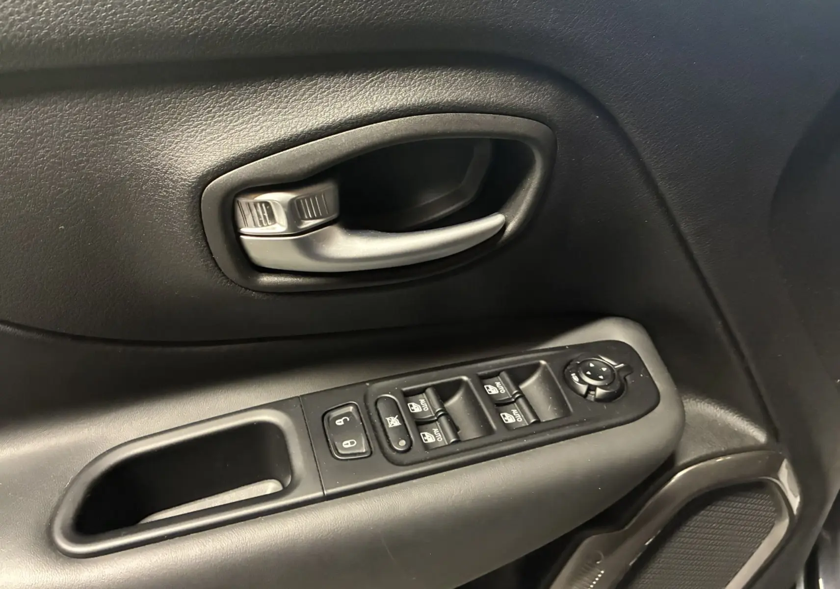 Gros plan sur la poignée intérieure et les commandes de lève-vitres côté gauche d’un Jeep Renegade noir 2019.