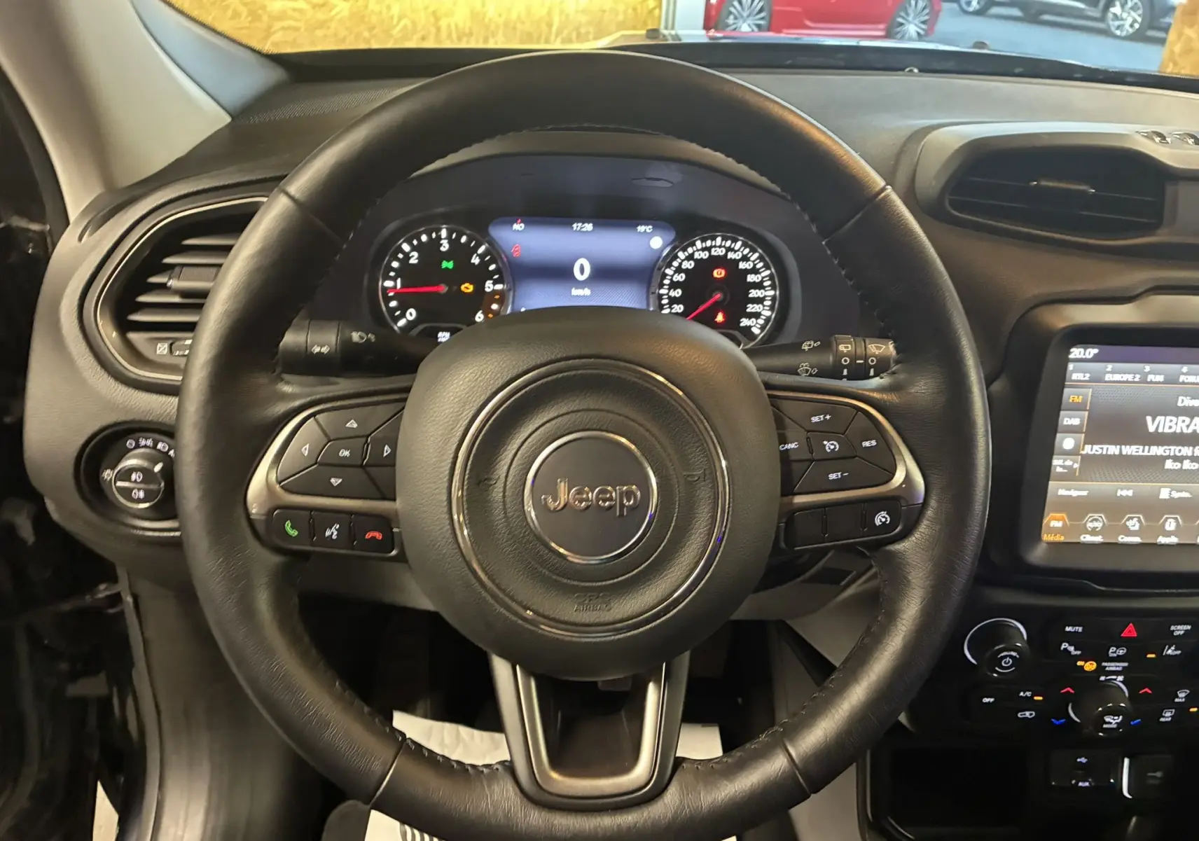 Vue intérieure centrée sur le volant en cuir noir du Jeep Renegade 2019 avec tableau de bord et écran tactile visible.