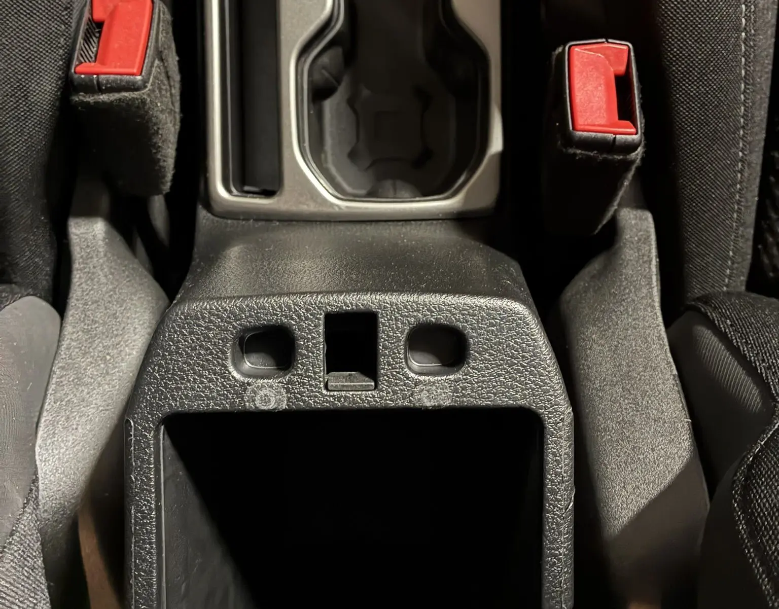 Gros plan sur la console centrale noire du Jeep Renegade 2019, montrant les ceintures de sécurité rouges et les porte-gobelets.