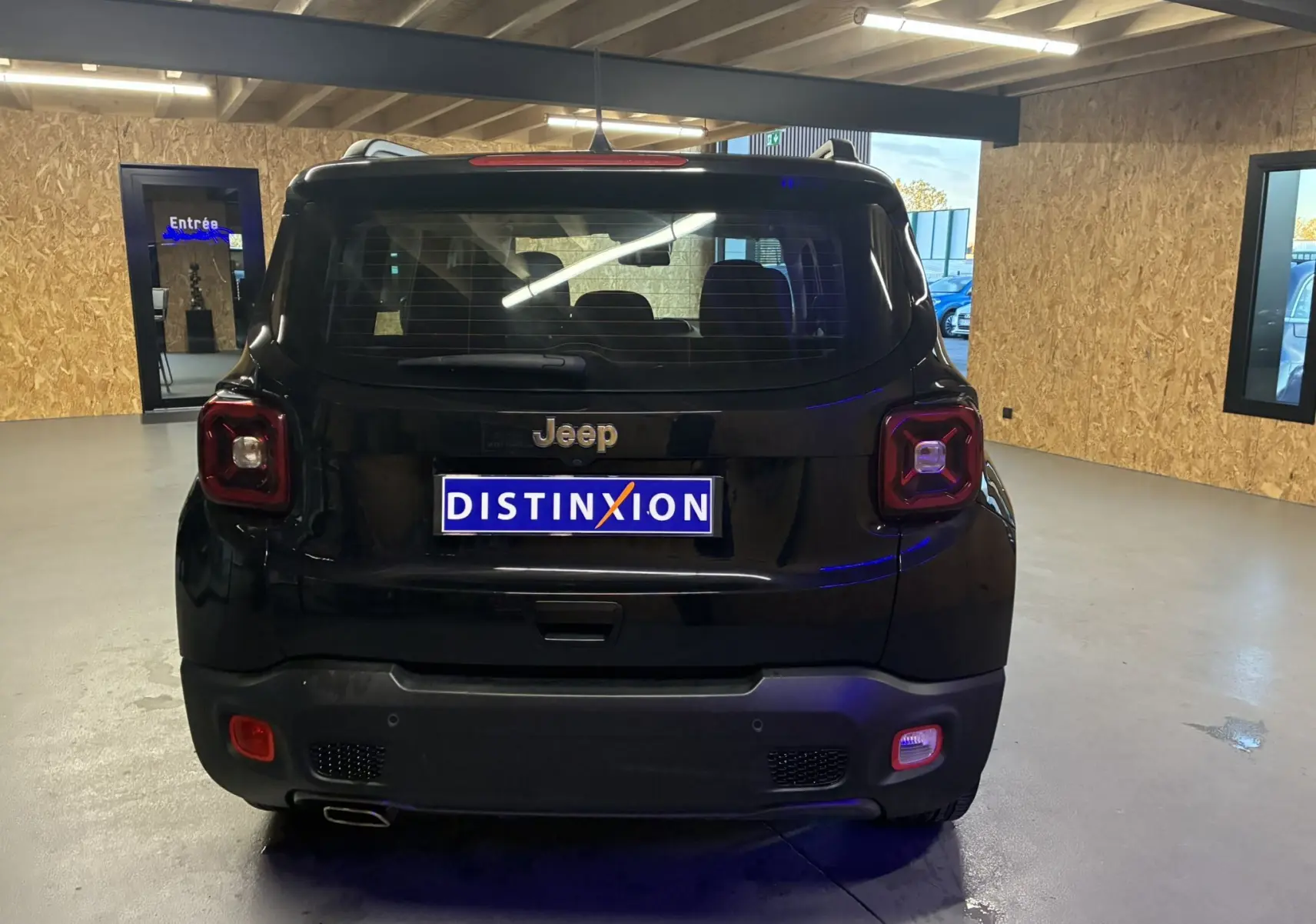 Vue arrière d'un Jeep Renegade noir 2019 en intérieur, avec feux arrière carrés et plaque Distinxion visible.