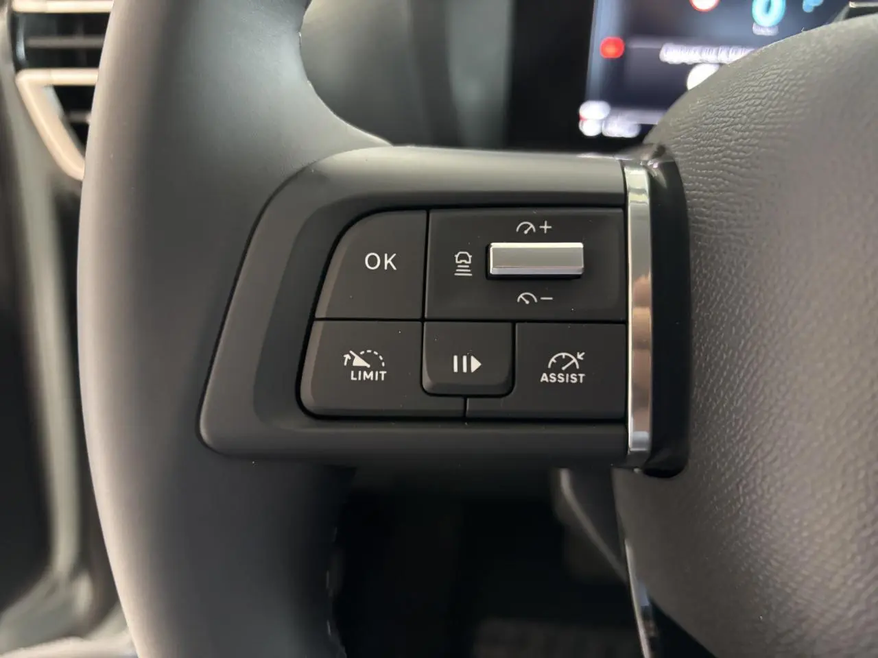Gros plan sur les commandes au volant à gauche du Citroën C4 hybride 2026, volant cuir noir.