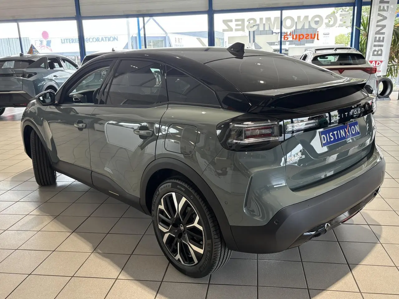 Vue 3/4 arrière droite d'une Citroën C4 hybride 2026 vert Manhattan avec toit noir et jantes alliage 18 pouces.