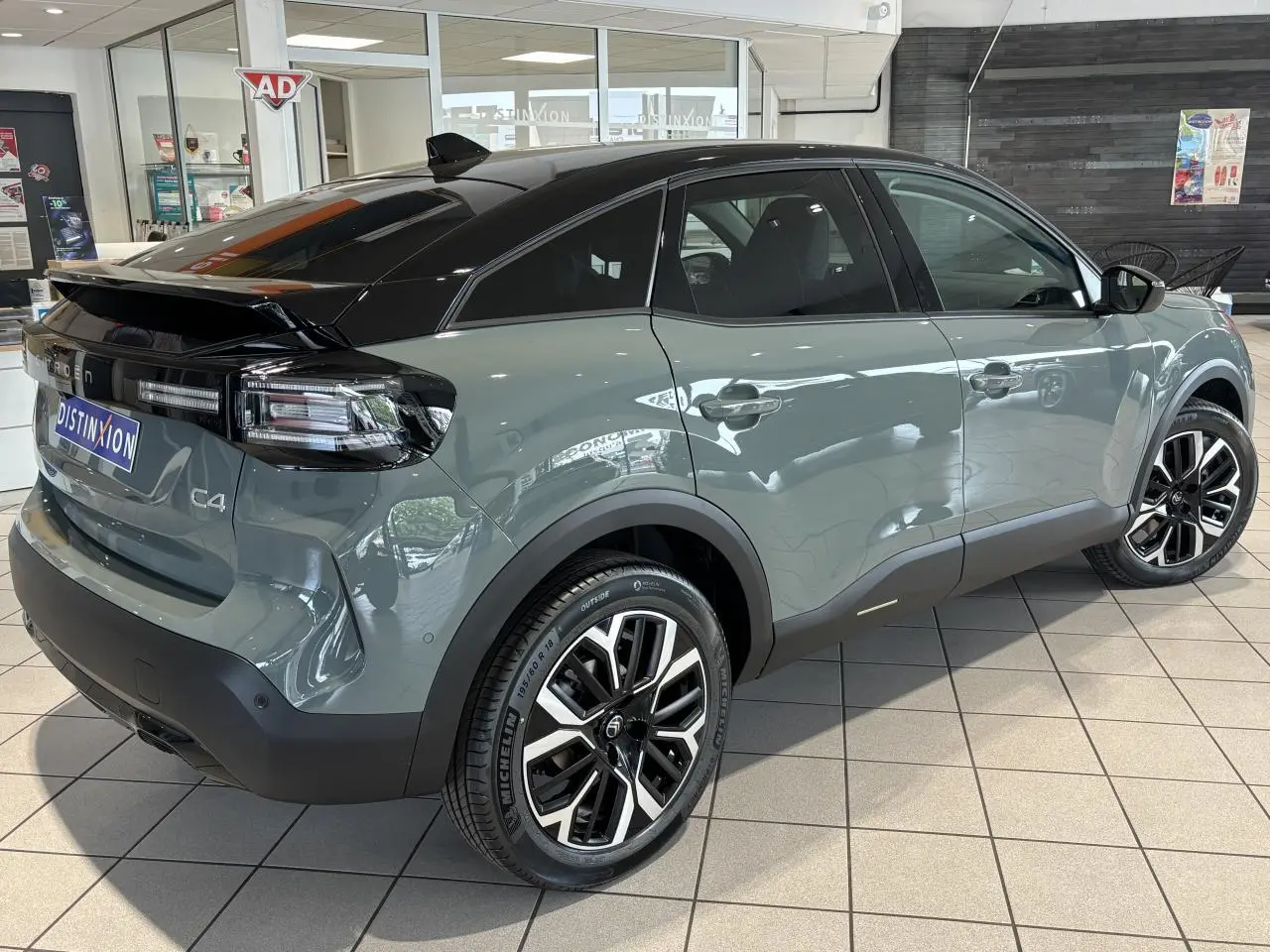 Vue 3/4 arrière droite d'une Citroën C4 2026 vert Manhattan avec toit noir Perla Nera et jantes alliage 18 pouces.