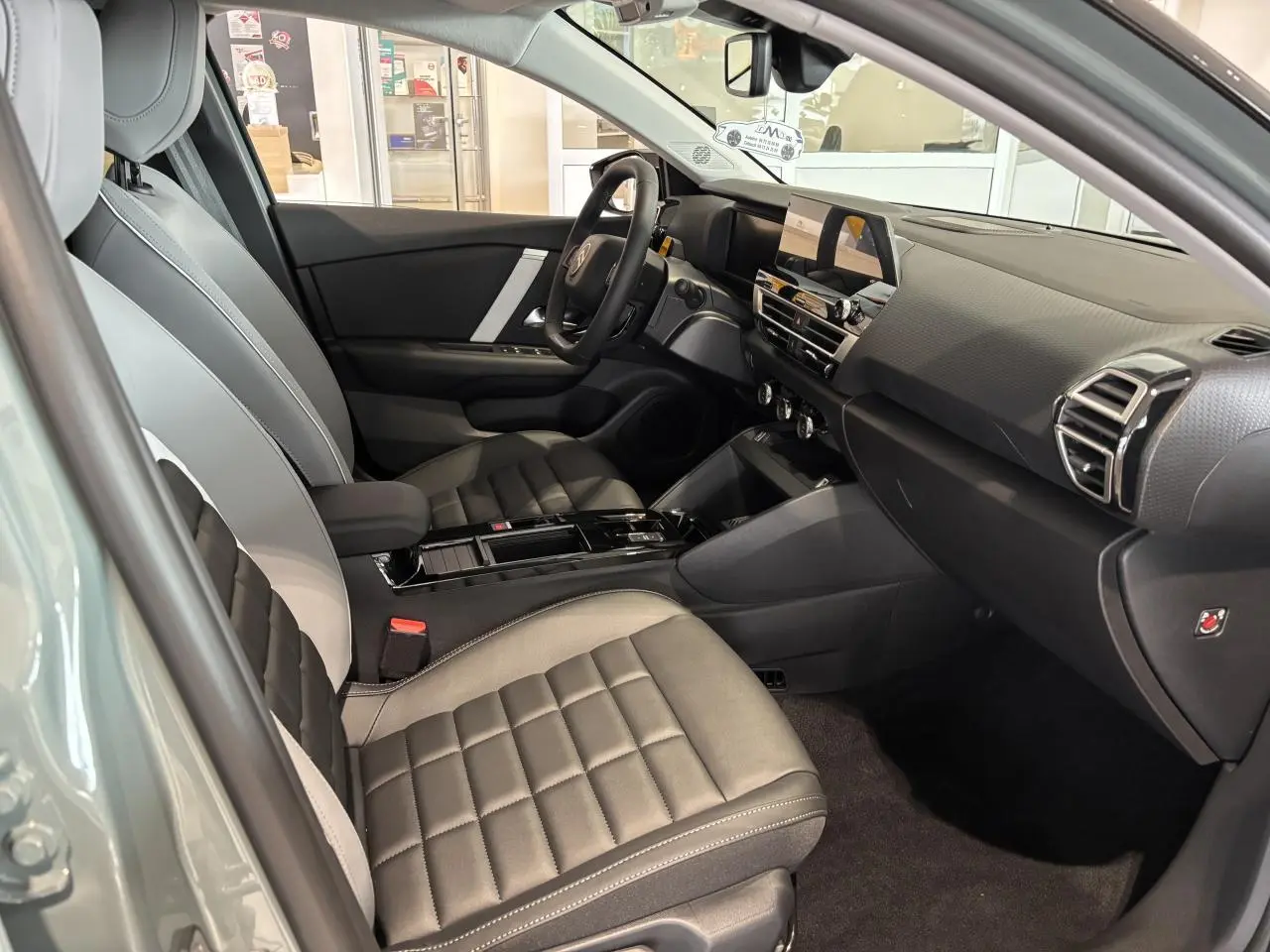 Intérieur avant droit de la Citroën C4 hybride 2026 avec sièges gris à surpiqûres et tableau de bord moderne noir.