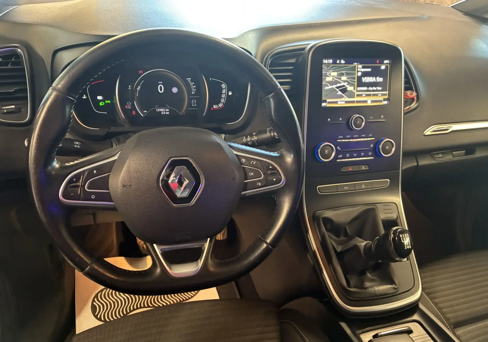 Vue intérieure du tableau de bord noir du Renault Grand Scenic 2017 avec volant cuir, écran tactile et levier de vitesse manuel.