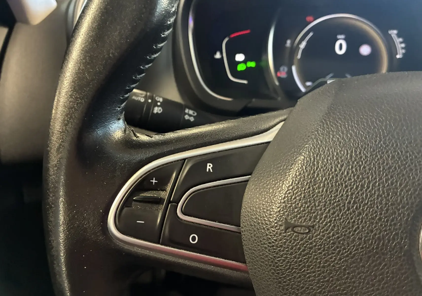 Gros plan sur le volant en cuir noir du Renault Grand Scenic 2017, avec commandes intégrées et tableau de bord numérique en arrière-plan.