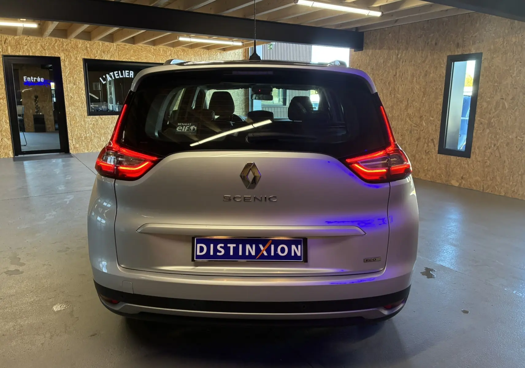 Vue arrière d'un Renault Grand Scenic gris 2017 avec feux allumés et logo Distinxion dans un garage.