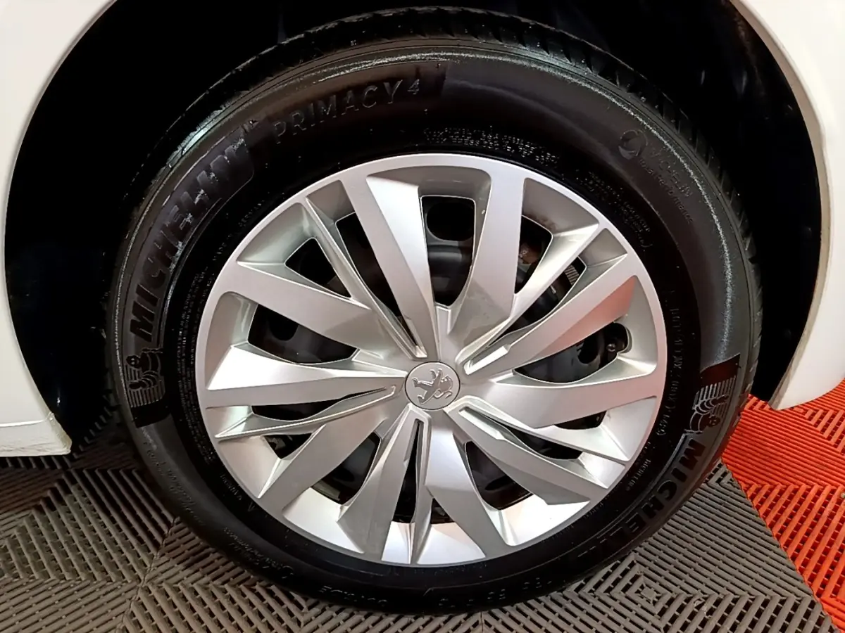 Gros plan sur la roue avant droite d'une Peugeot 208 blanche, mettant en valeur la jante alu et le pneu Michelin.