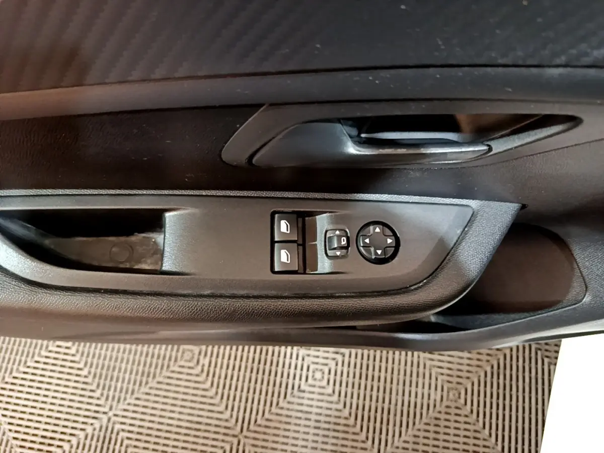 Vue rapprochée de la commande des vitres et rétroviseurs sur la porte intérieure noire d'une Peugeot 208 blanche.