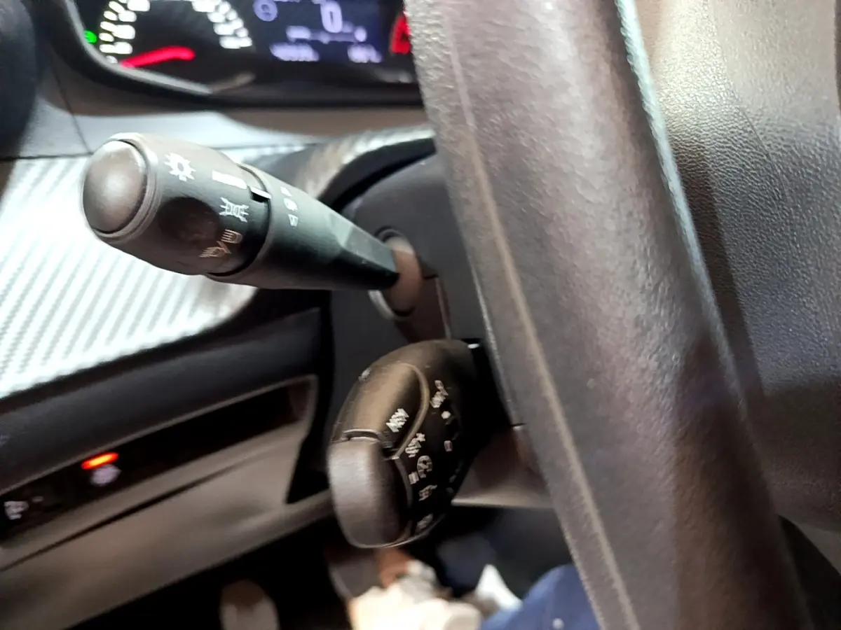 Gros plan sur les commandes au volant et le tableau de bord noir de la Peugeot 208 blanche, version 1.5 BlueHDi 100 S&S Premium.