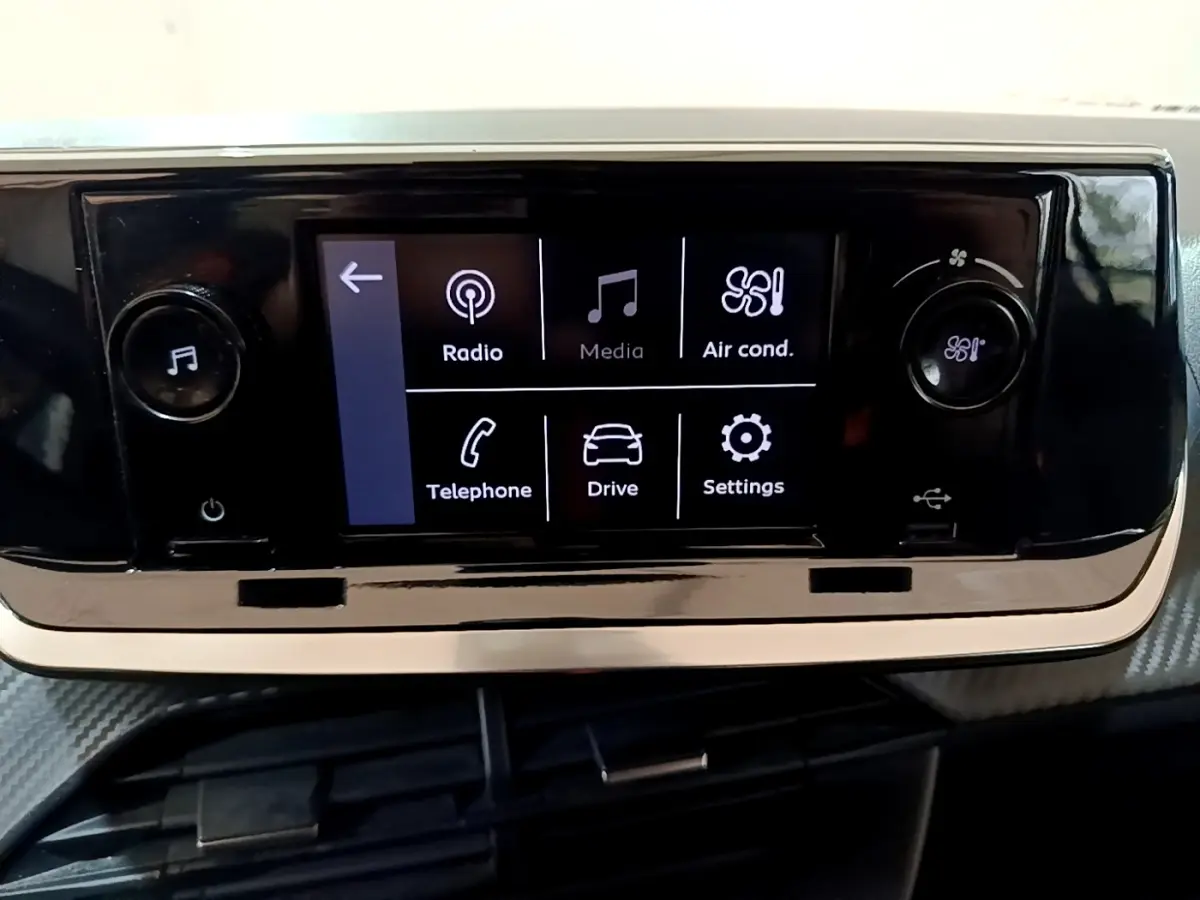 Écran tactile central noir affichant les options radio, média, climatisation, téléphone, conduite et réglages dans une Peugeot 208.