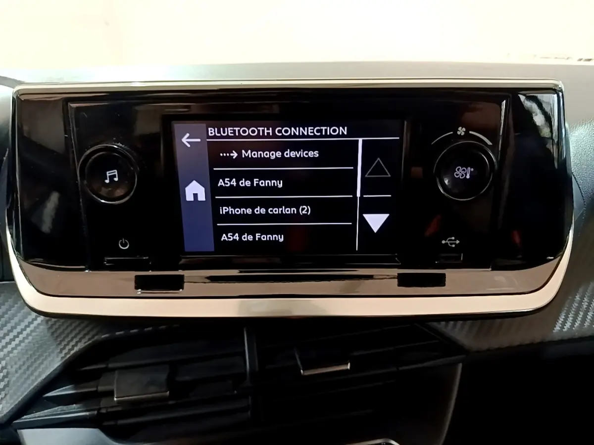 Écran tactile central noir affichant la connexion Bluetooth dans l'habitacle d'une Peugeot 208 blanche, vue de face.