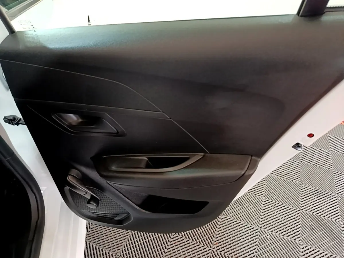 Vue intérieure de la porte avant gauche noire d’une Peugeot 208 blanche, avec poignée et commande de vitre manuelle.