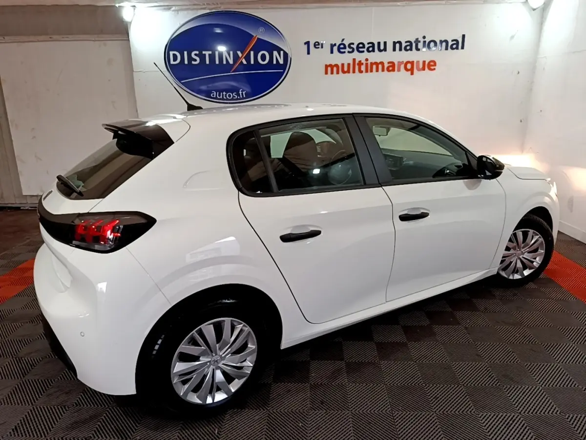 Vue 3/4 arrière droite d'une Peugeot 208 blanche 2022, avec jantes alliage et vitres teintées en intérieur showroom.
