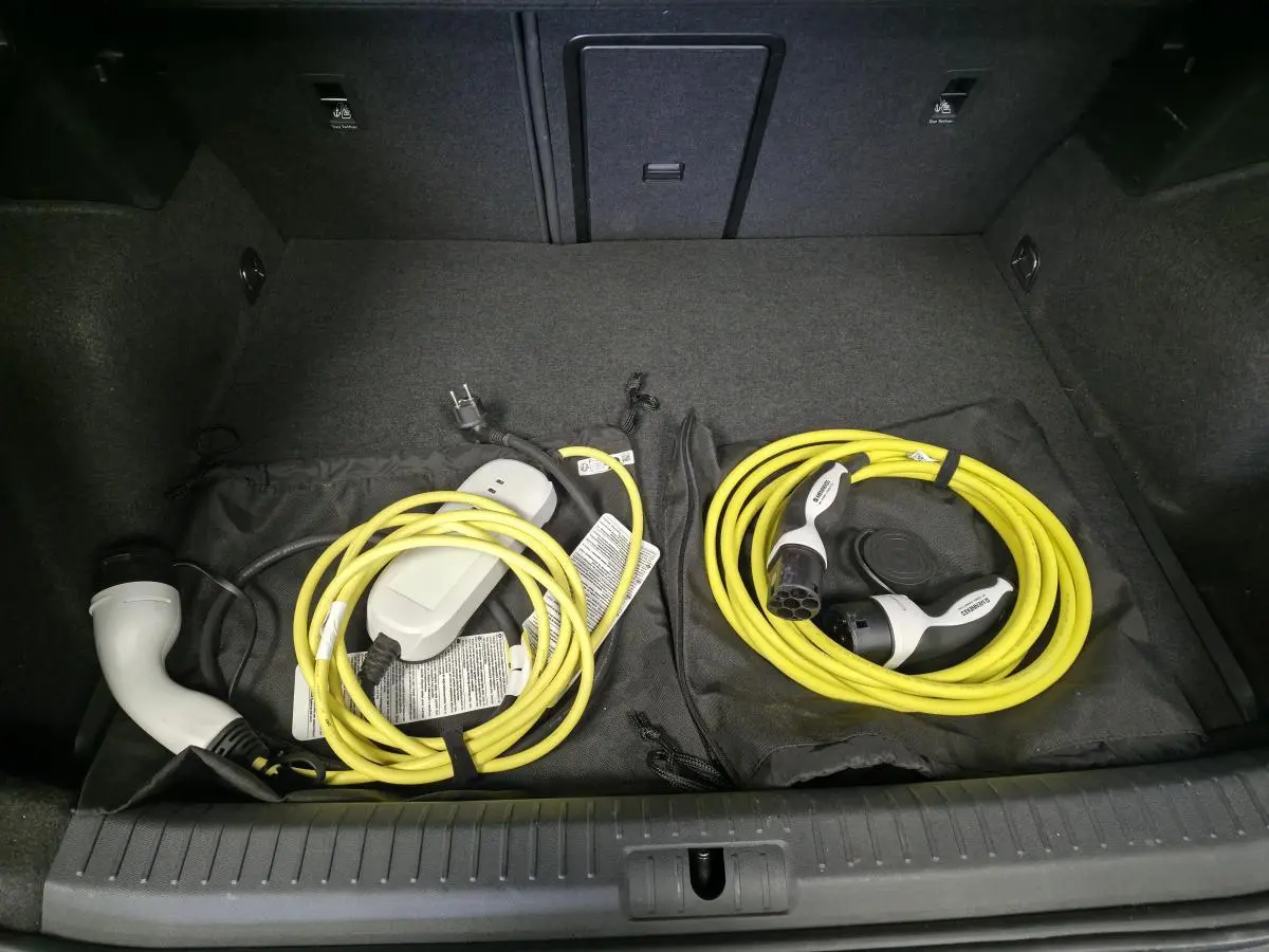 Coffre ouvert d'une CUPRA Formentor 1.4 e-Hybrid 2023 avec câbles de recharge jaune rangés sur tapis noir.