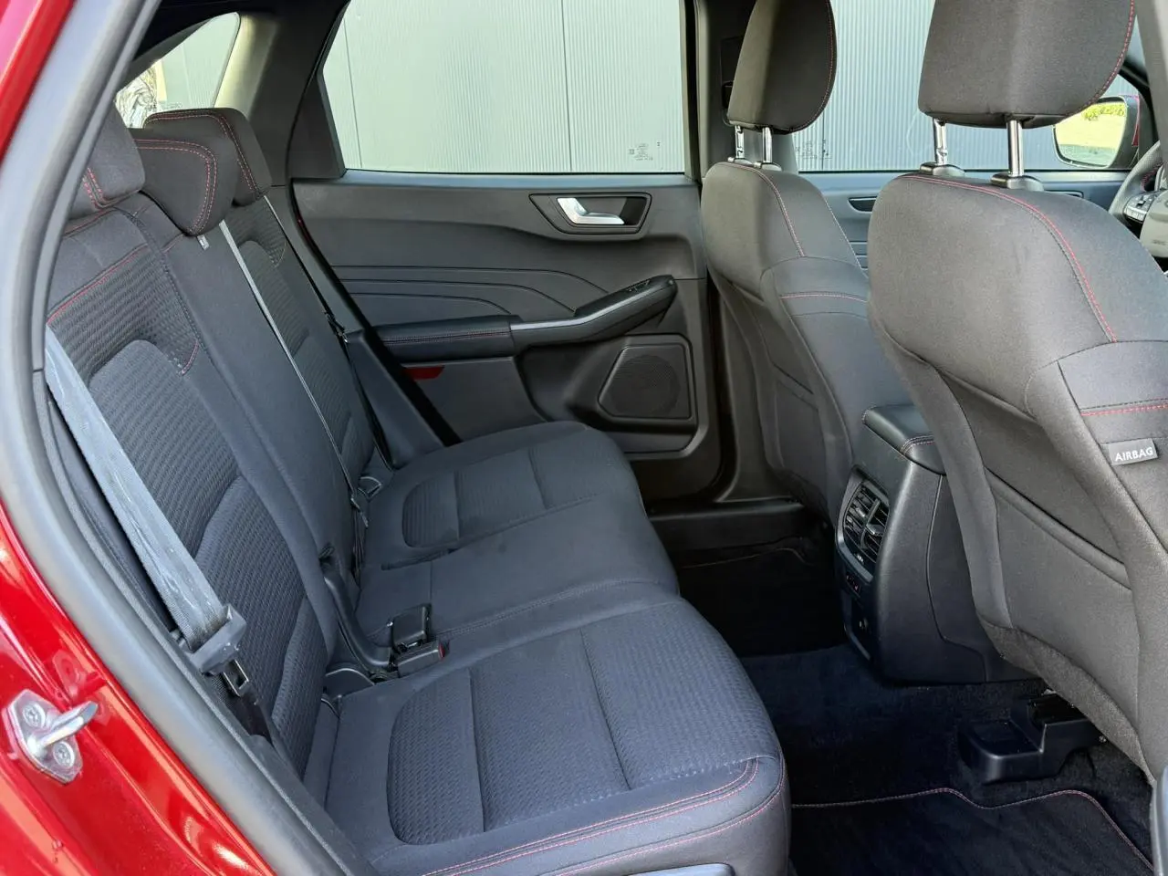 Vue intérieure arrière côté gauche du Ford Kuga rouge Lucifer 2024, sièges tissu noir avec surpiqûres rouges et appuie-têtes réglables.