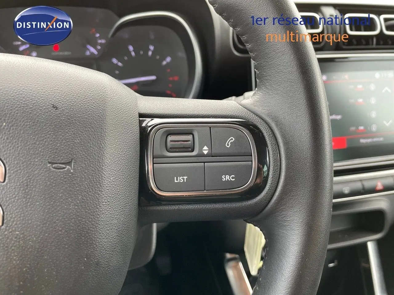 Gros plan sur les commandes au volant noir du Citroën C3 Aircross 2023, avec tableau de bord et écran tactile en arrière-plan.