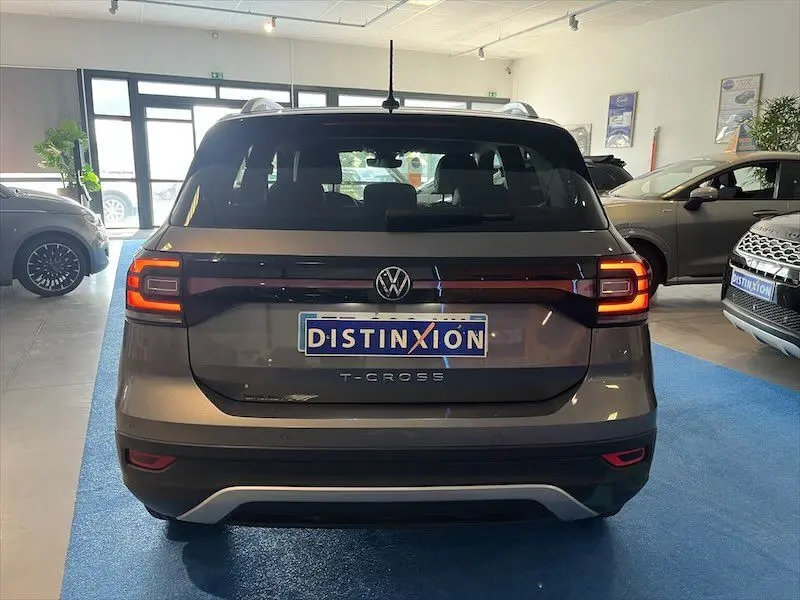 Vue arrière d'un Volkswagen T-Cross gris Limestone métallisé dans un showroom avec éclairage naturel.