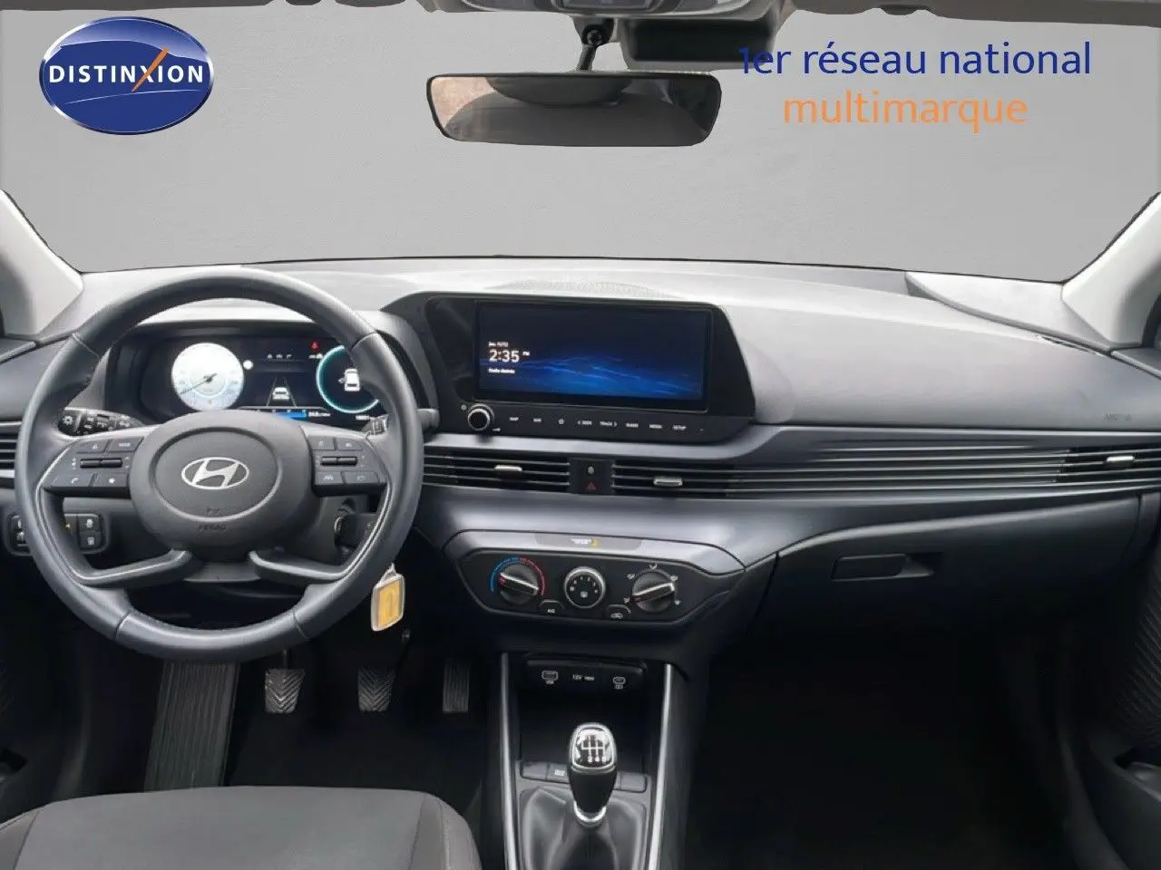 Vue intérieure avant du tableau de bord gris d'une Hyundai i20 2025 avec volant cuir multifonction et écran tactile central.