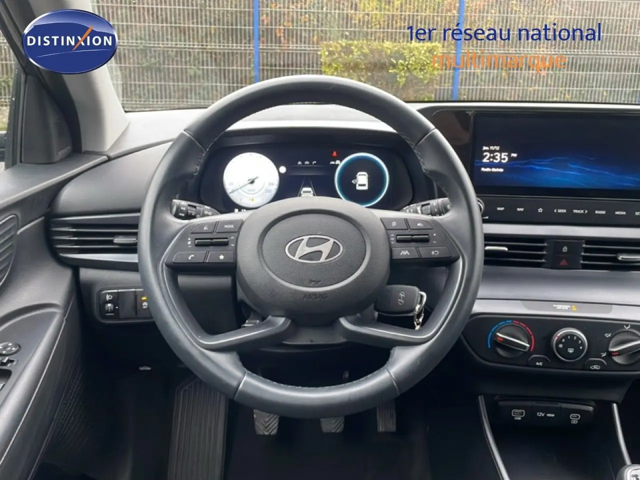 Vue intérieure centrée sur le volant cuir noir d’une Hyundai i20 2025, avec tableau de bord numérique et écran tactile.
