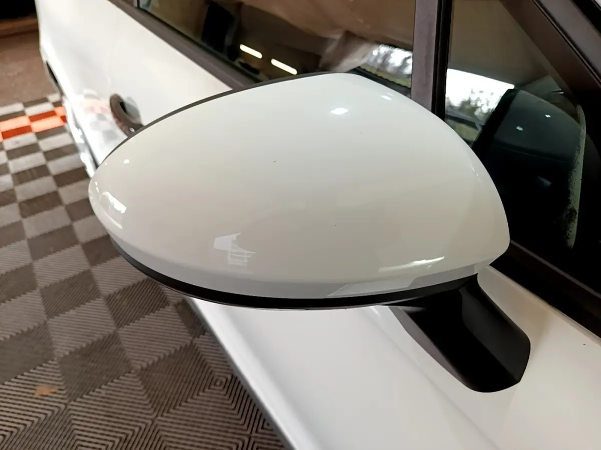 Gros plan sur le rétroviseur côté gauche blanc d'une Renault Clio Business 2021, avec portière et vitre visibles.