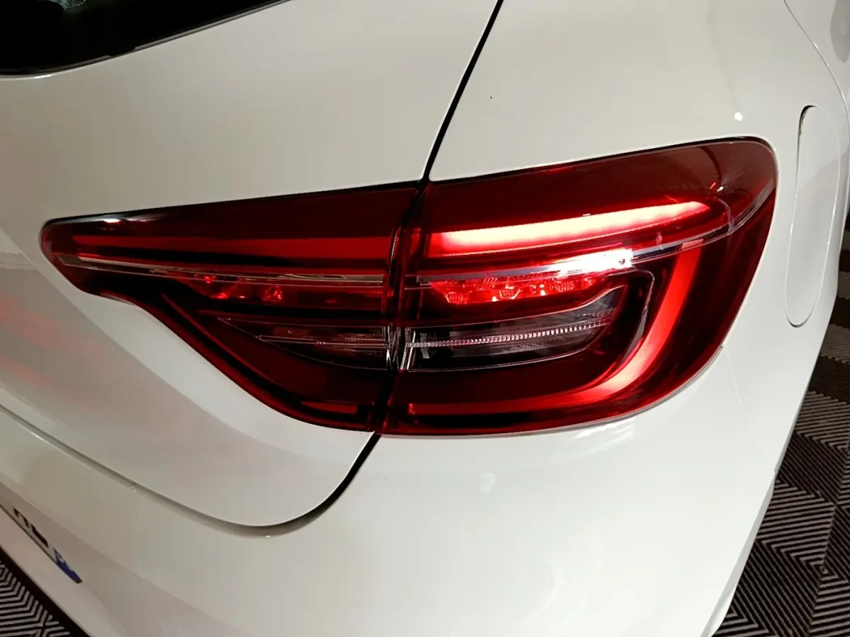 Gros plan sur le feu arrière droit rouge d’une Renault Clio Business blanche, vue de l’arrière côté droit.