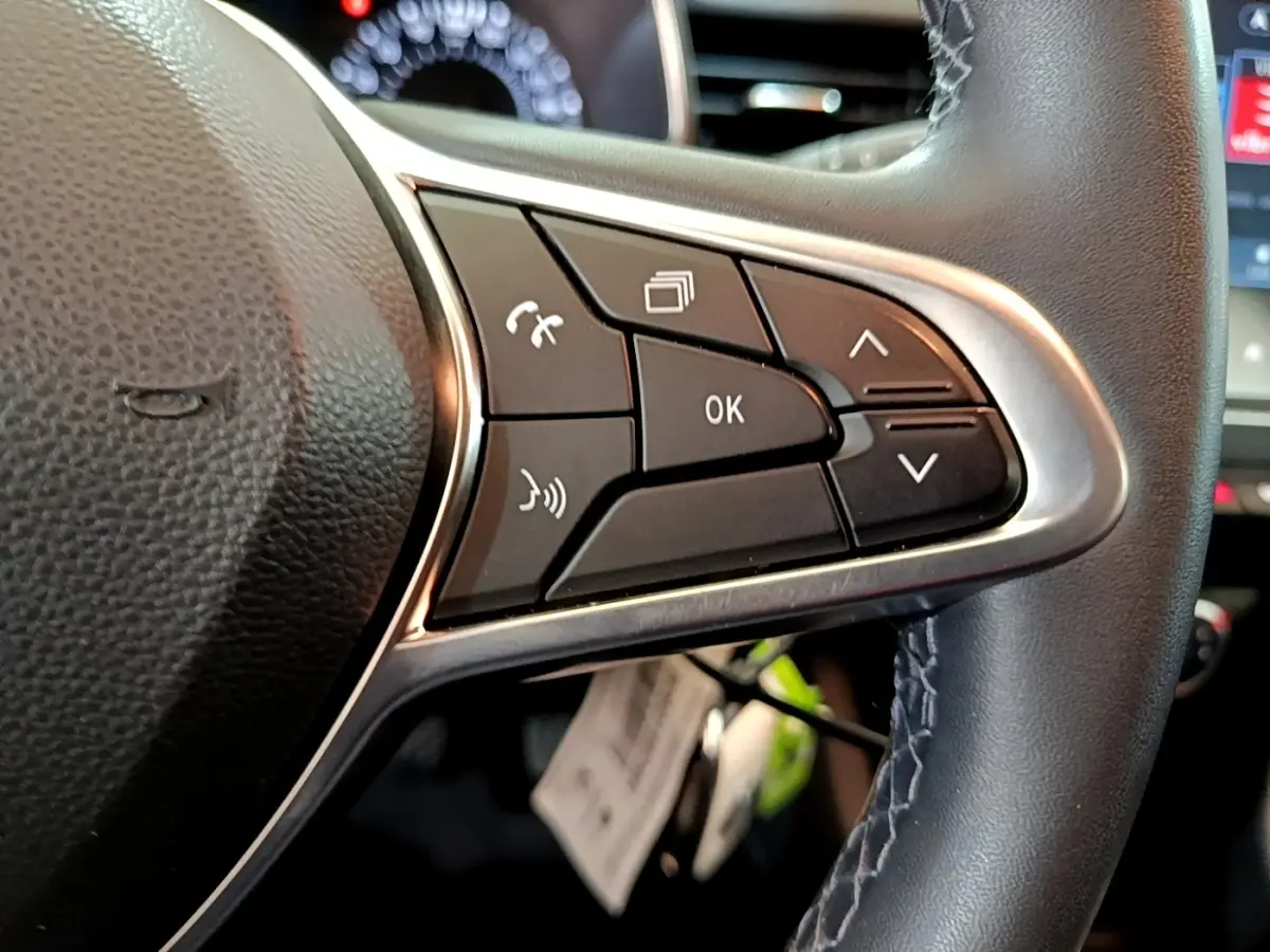 Gros plan sur les commandes multifonctions à droite du volant cuir noir de la Renault Clio Business blanche de 2021.