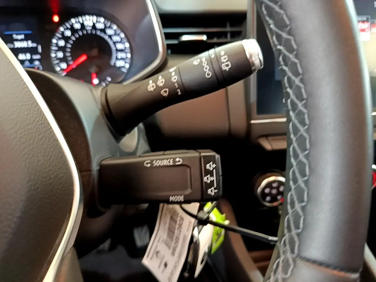 Gros plan sur la commande multifonction et le volant cuir de la Renault Clio Business blanche, tableau de bord en arrière-plan flou.