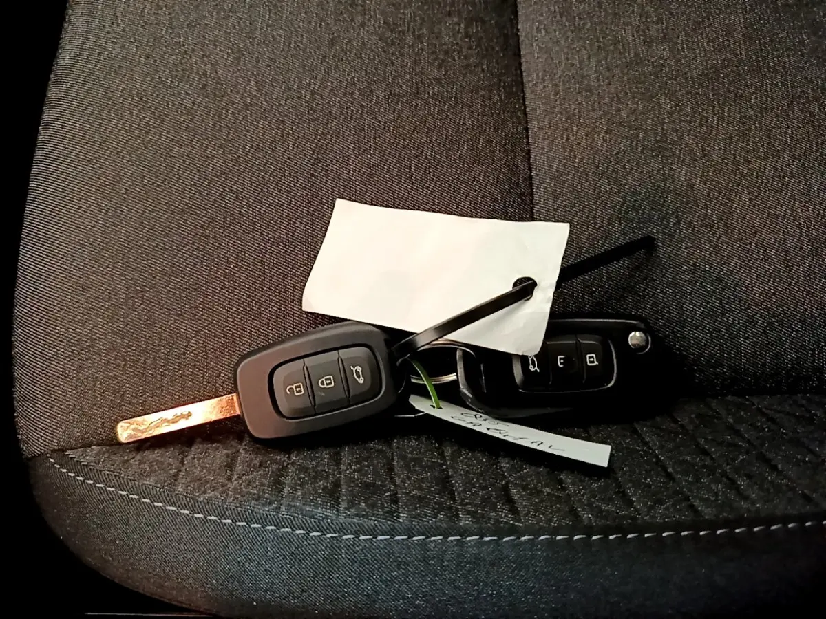 Clé de voiture Renault Clio Business blanche posée sur un siège tissu gris foncé, vue rapprochée.