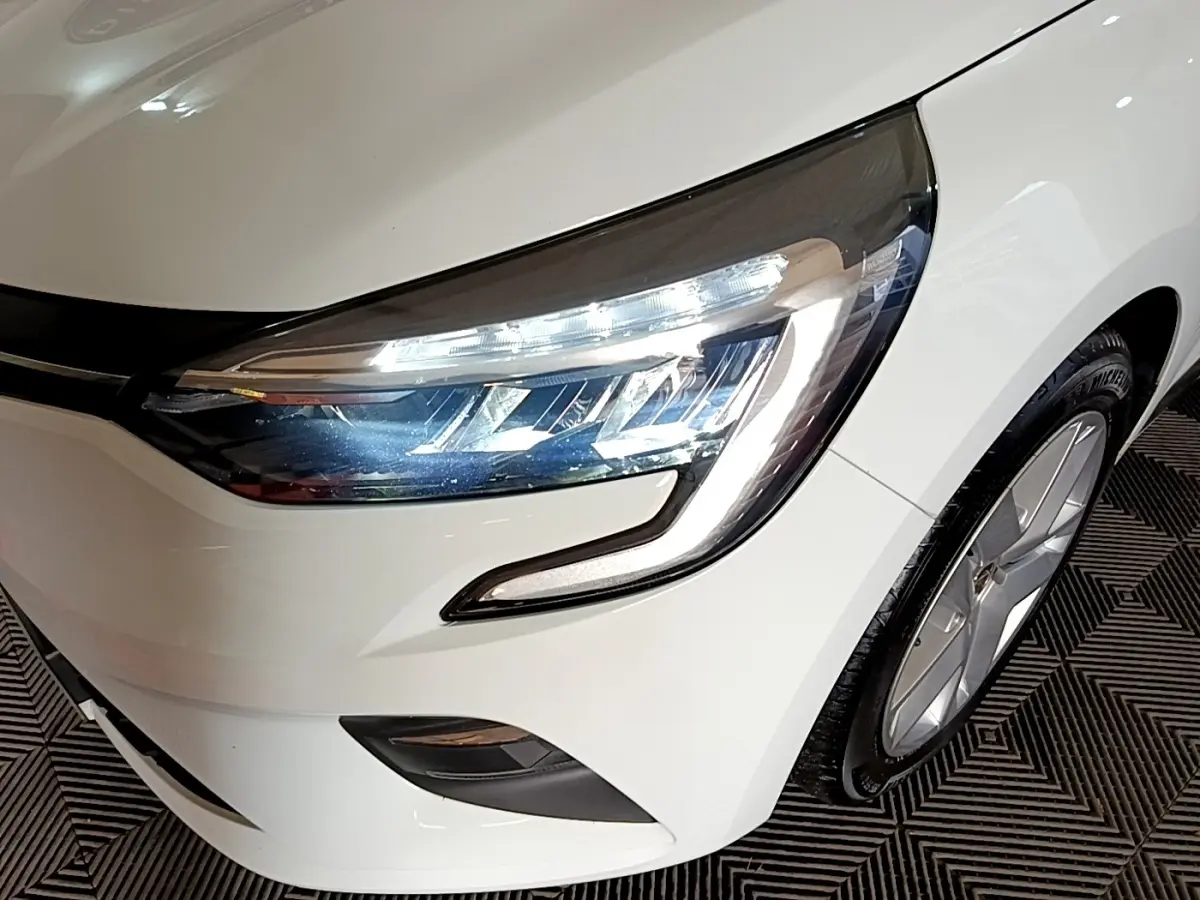 Gros plan sur l'avant droit blanc d'une Renault Clio 2021, mettant en valeur le phare LED et la jante alu.