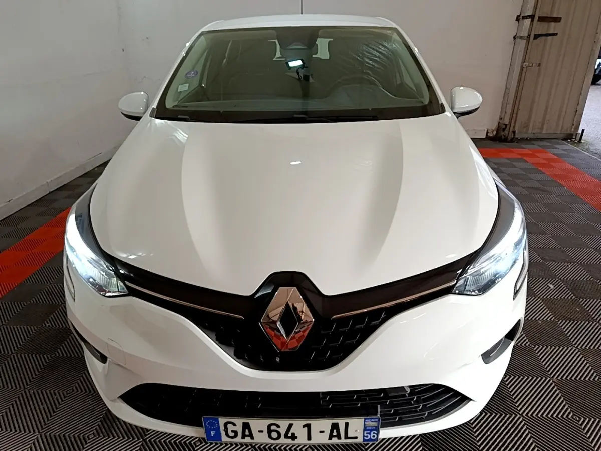 Vue avant d'une Renault Clio blanche 2021 avec phares LED allumés et calandre noire brillante.