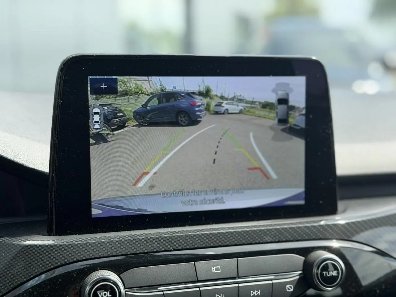 Écran intérieur montrant la caméra de recul avec vue arrière sur un Ford Kuga gris Solar en stationnement.