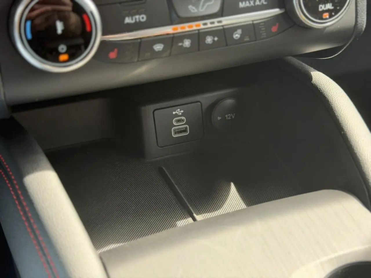 Gros plan sur la console centrale du Ford Kuga ST-Line 2024, montrant ports USB et prise 12V avec surpiqûres rouges.