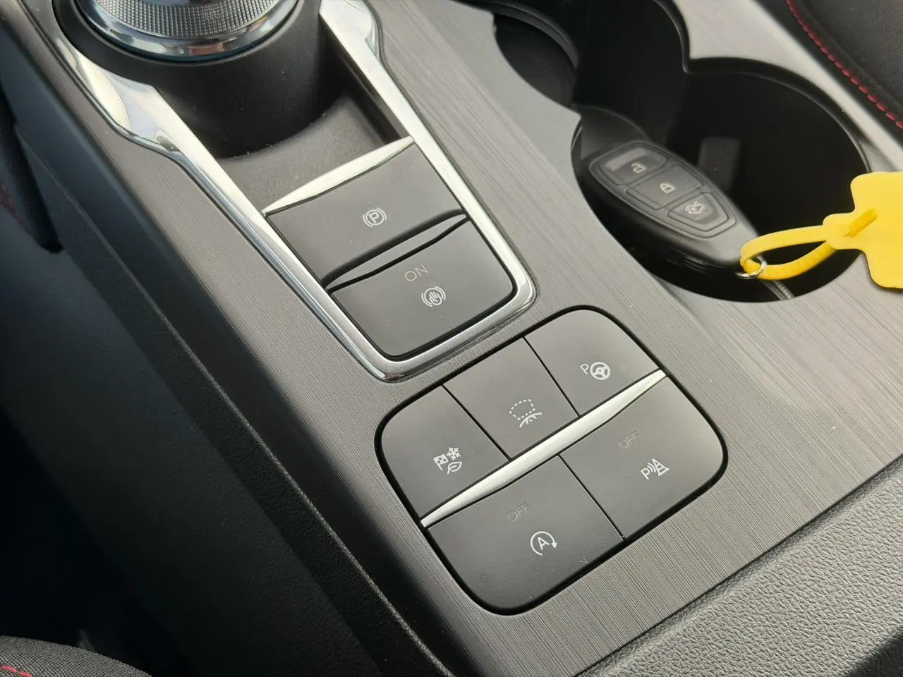 Vue rapprochée de la console centrale du Ford Kuga 2024 gris Solar, avec boutons de contrôle et clé dans porte-gobelets.