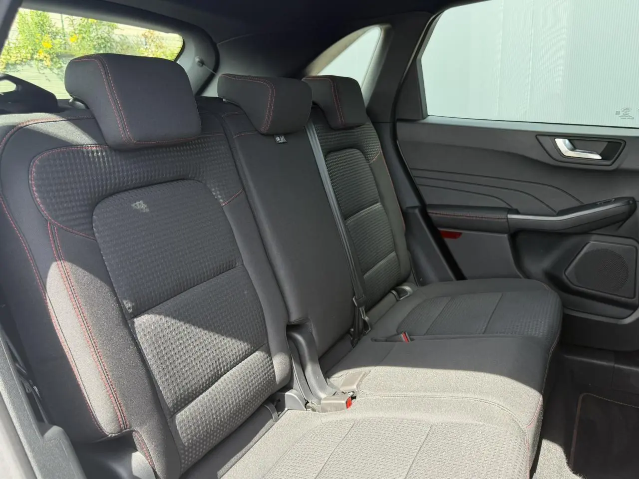 Vue latérale intérieure sur les sièges arrière noirs avec surpiqûres rouges du Ford Kuga 2024 finition ST-Line.