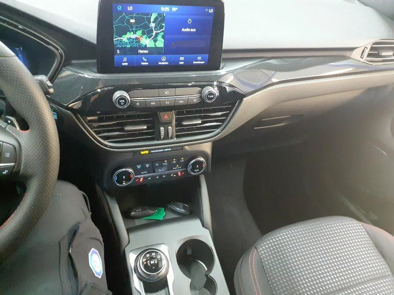 Vue intérieure du Ford Kuga 2024, tableau de bord et console centrale avec écran tactile et sélecteur rotatif gris.