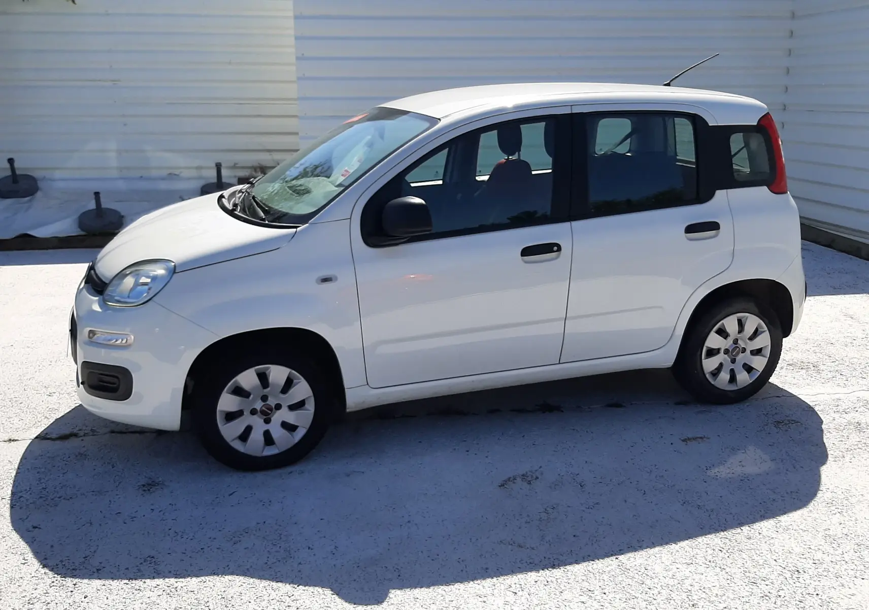 Vue 3/4 avant droite d'une Fiat Panda blanche 2018 essence avec plaque "OCCASION" et intérieur rouge visible.
