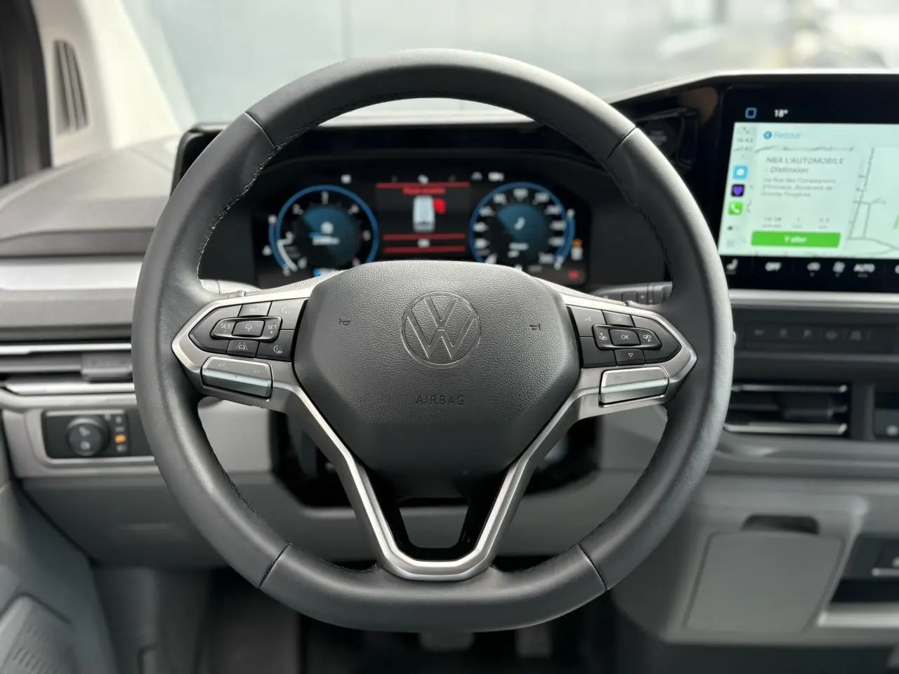 Vue rapprochée du volant multifonction en similicuir noir du Volkswagen Transporter T7 avec tableau de bord digital et écran tactile.