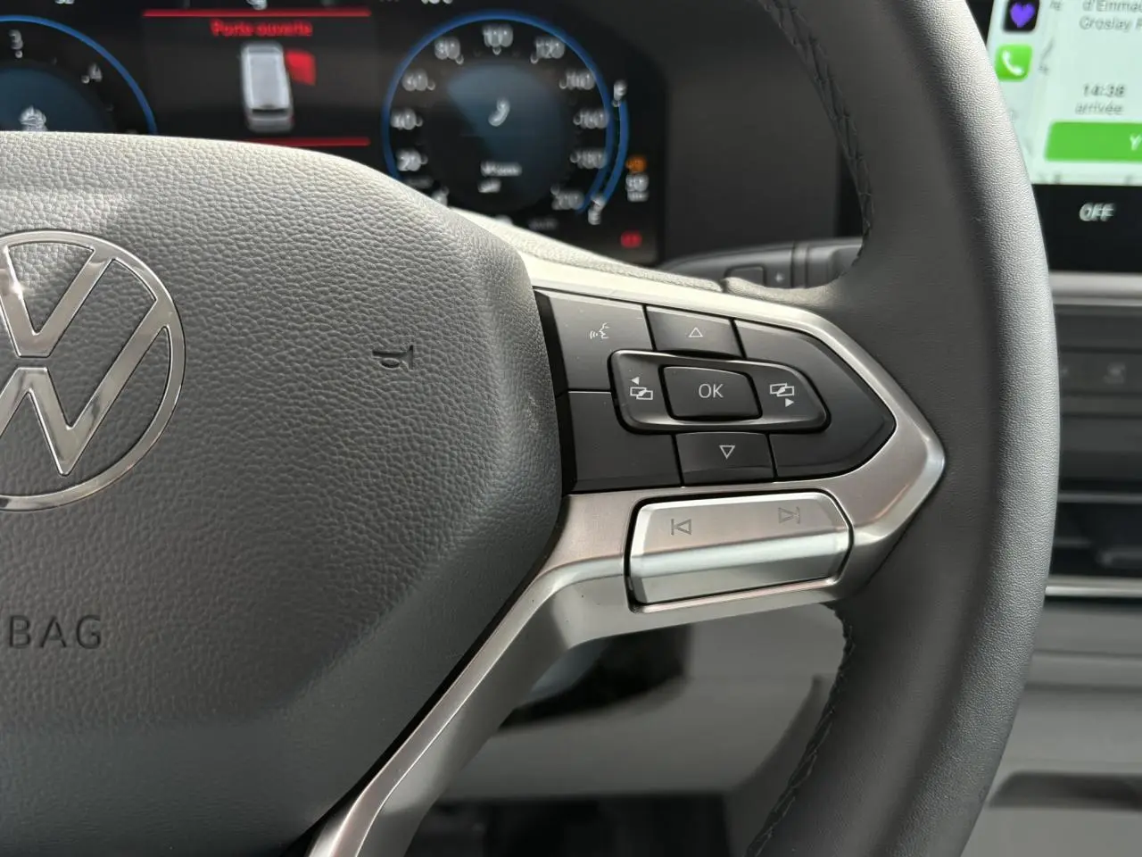 Gros plan sur le volant multifonction noir du Volkswagen Transporter T7 avec commandes intégrées et tableau de bord numérique en arrière-plan.