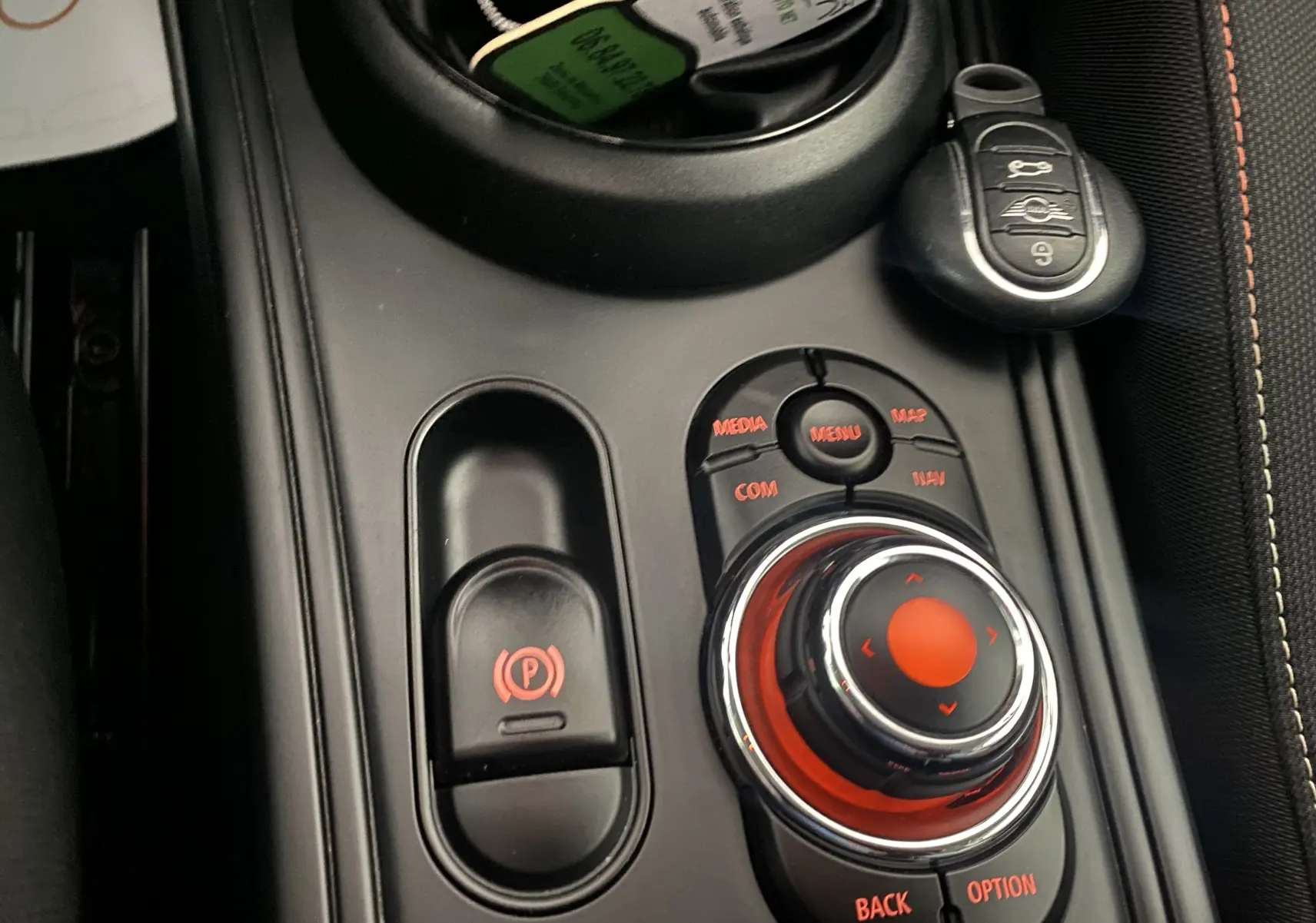Gros plan sur la console centrale noire du MINI Countryman rouge, avec molette de contrôle et clé intelligente visible.