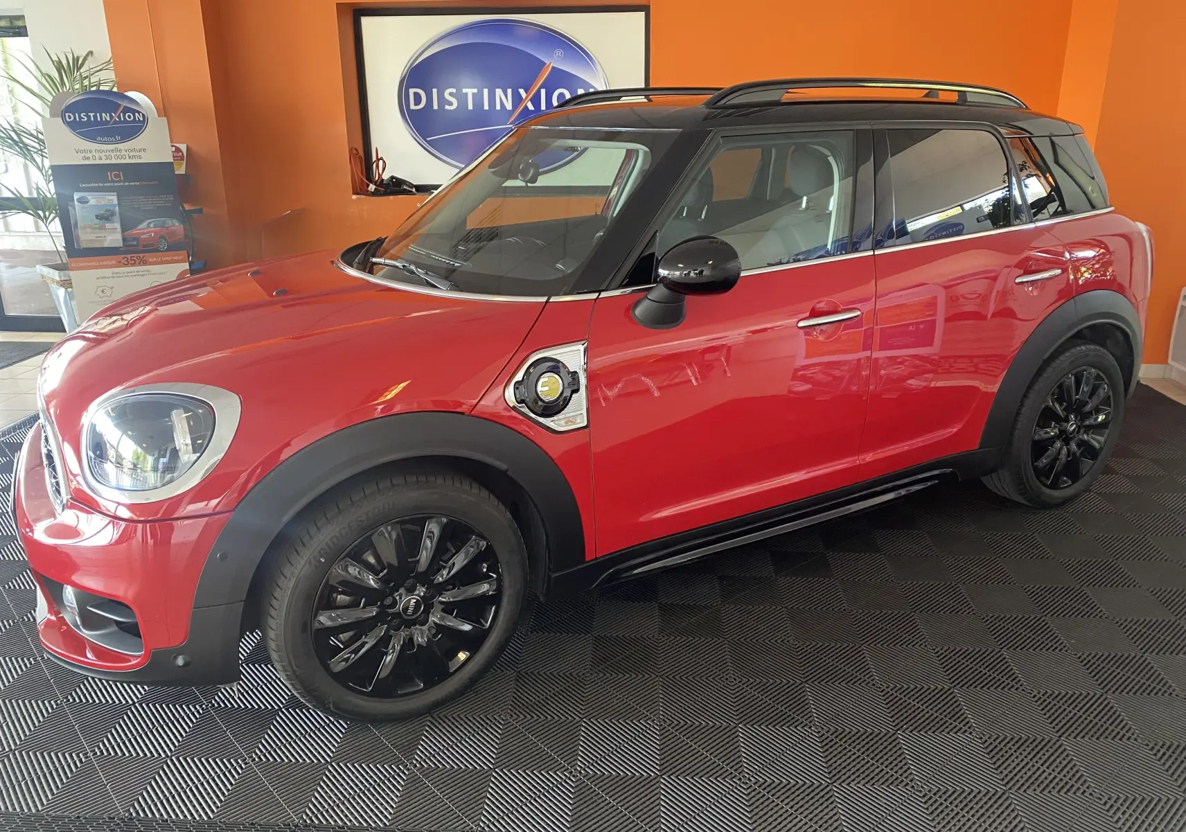 Vue de profil côté gauche d'une MINI Countryman Cooper SSE rouge avec toit noir et jantes noires en intérieur showroom.