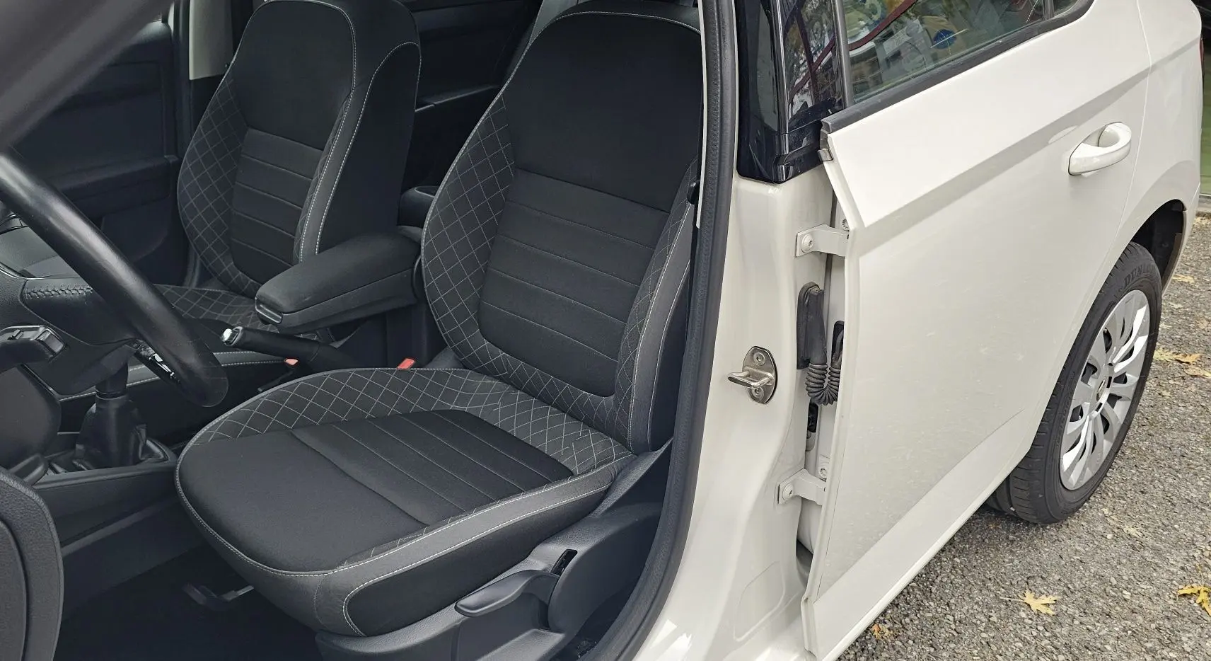 Vue intérieure côté conducteur d'une Skoda Fabia blanche cristal, mettant en valeur la sellerie Business noire satin avec surpiqûres grises.