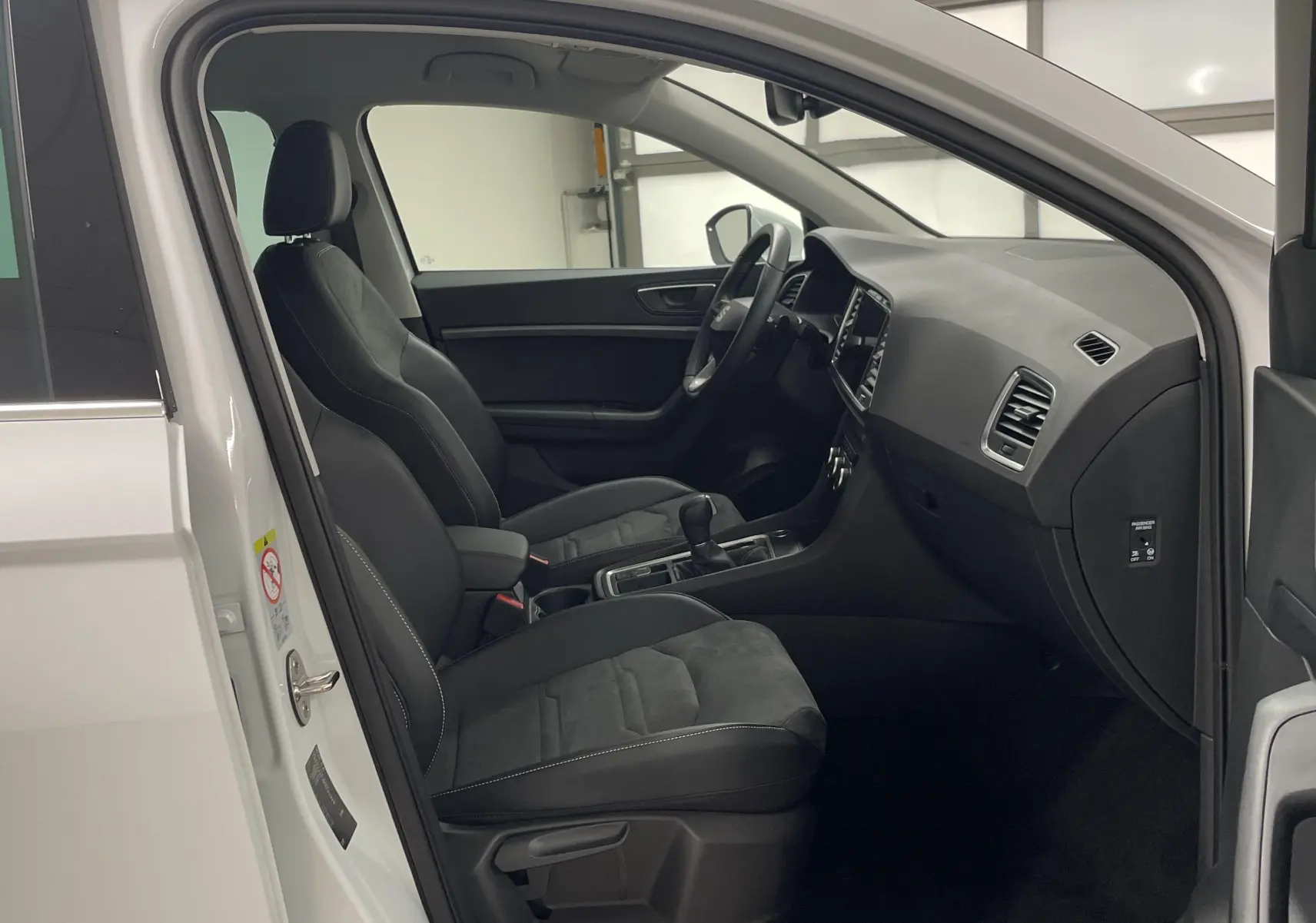 Intérieur du SEAT Ateca blanc Nevada 2024 vu côté gauche, sièges noirs et tableau de bord moderne visible.