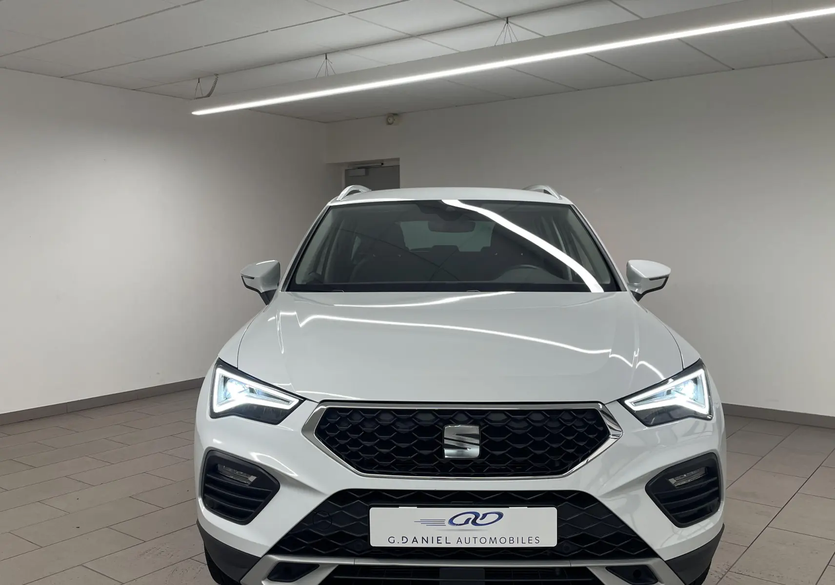 Vue avant d'un SEAT Ateca blanc Nevada 2024 avec phares LED allumés et calandre hexagonale noire.