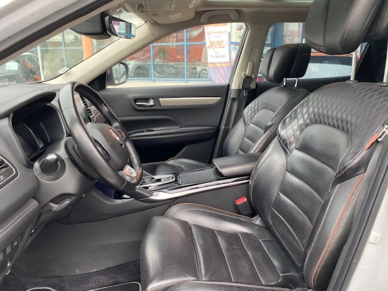 Intérieur du Renault Koleos blanc 2019, vue côté conducteur, sièges cuir noir avec surpiqûres orange et tableau de bord moderne.