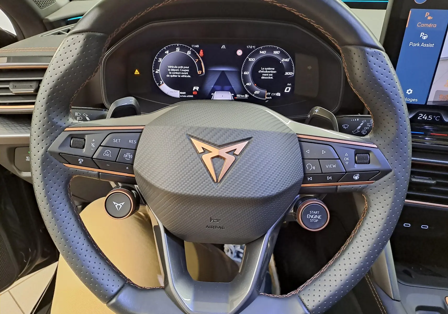 Vue rapprochée du volant perforé avec logo cuivré du CUPRA Leon 2025, tableau de bord digital et commandes intégrées.