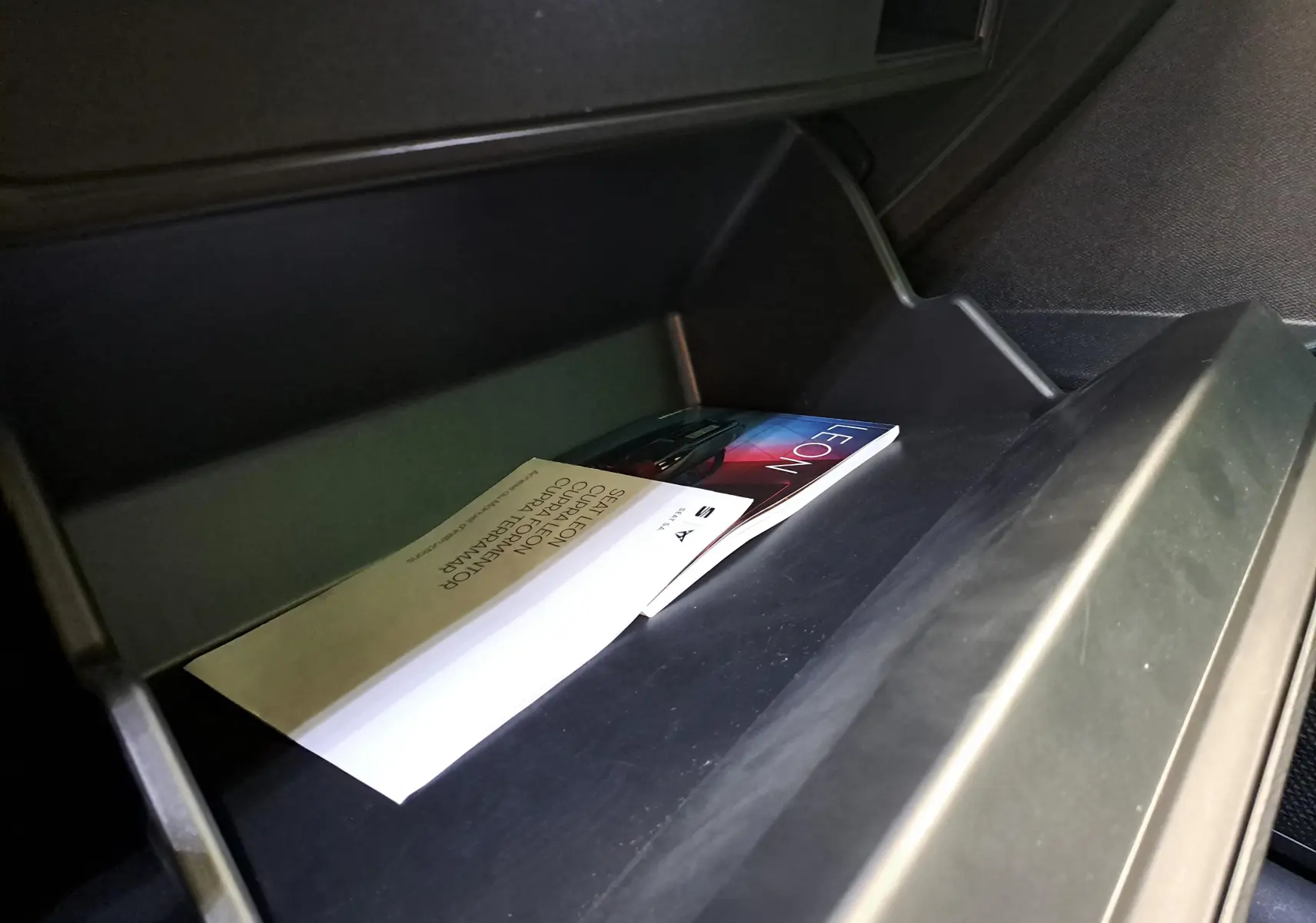 Gros plan sur la boîte à gants ouverte d'une CUPRA Leon Ph.2 2025, contenant des manuels et documents d'origine.