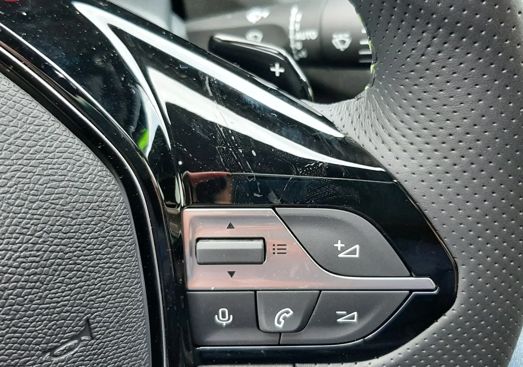 Gros plan sur les commandes gauche du volant perforé de la Peugeot 308 Hybrid 2026, finition noire brillante.
