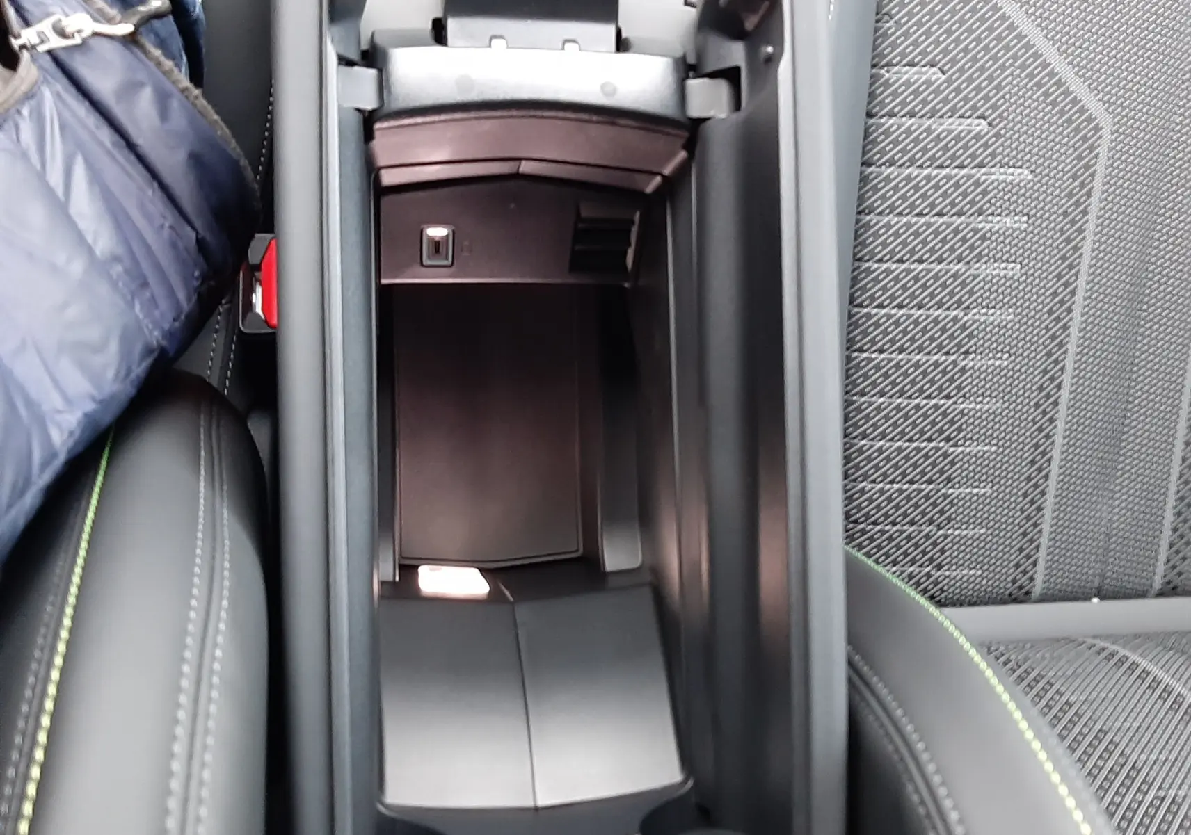 Vue intérieure en plongée du rangement central ouvert de la Peugeot 308 Hybrid 1.2 GT, avec sellerie noire et surpiqûres vertes.