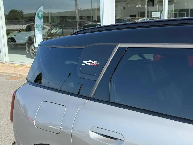 Vue latérale arrière droite d'une MINI Countryman JCW argentée avec toit noir et logo John Cooper Works sur la vitre arrière.